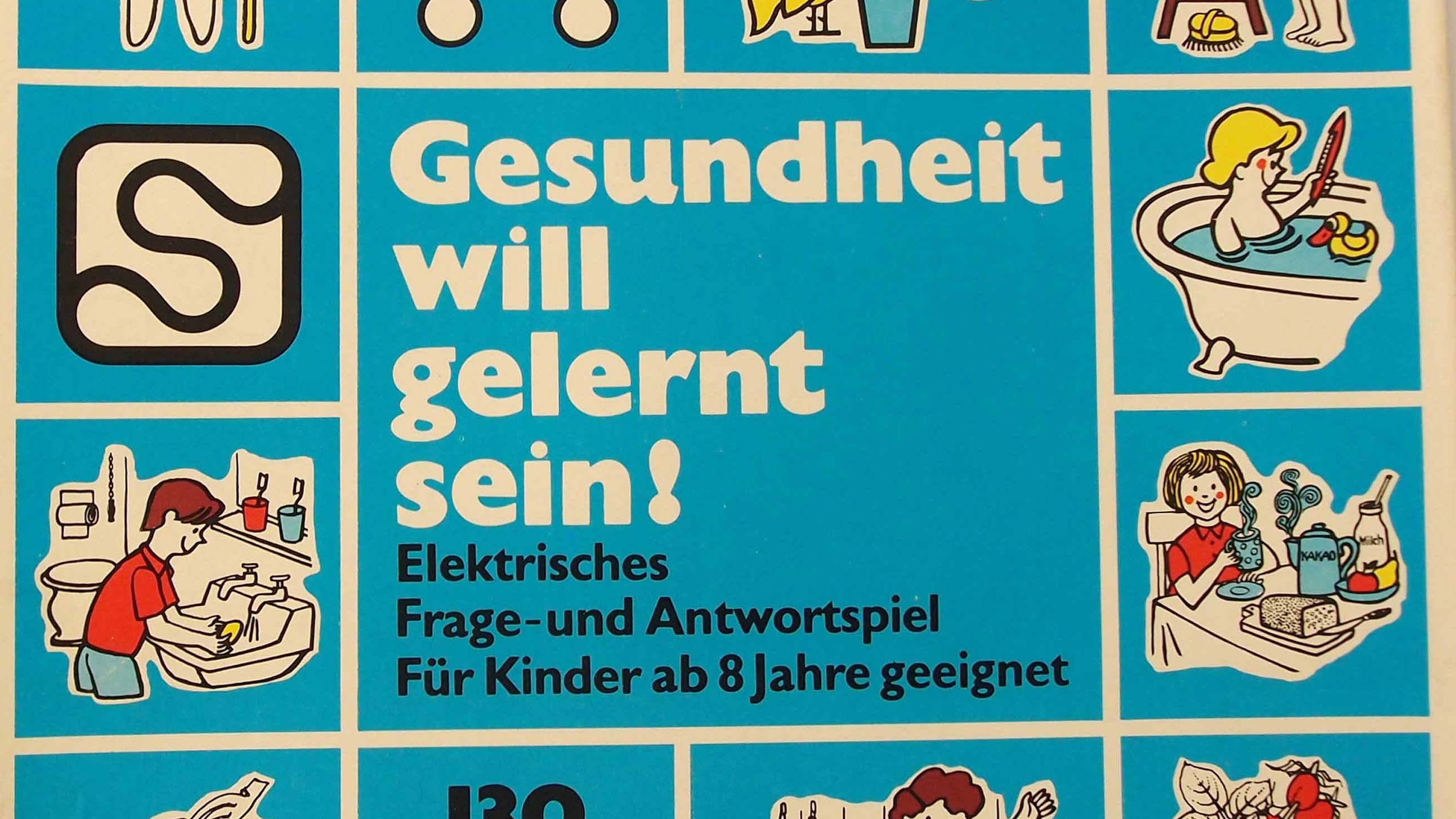 Foto: Ausschnitt einer Spielschachtel mit Illustrationen - ein Kind bei der Hausarbeit, beim Frühstücken und beim Baden. Aufschrift "Gesundheit will gelernt sein! Elektrisches Frage- und Antwortspiel Für Kinder ab 8 Jahre geeignet"
